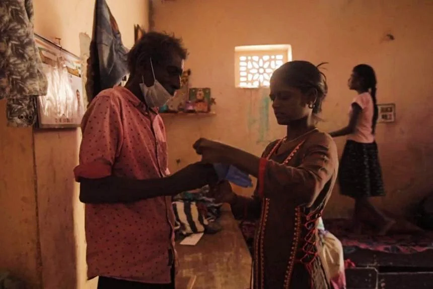 Mr Munisamy's teenage granddaughter Chandana helping him put on his gloves before he heads out for work. Photo: Arvind Dev.